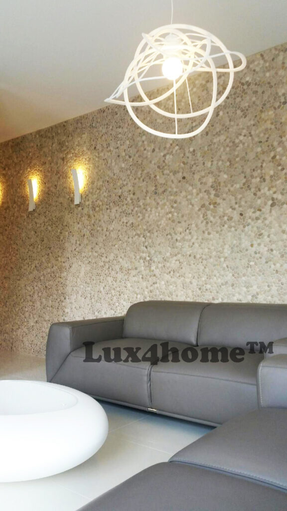 Mozaika z otoczaków MALUKU TAN na ścianie apartamentu 12 Mozaika MALUKU TAN za szarą sofą w salonie z wiszącą lampą